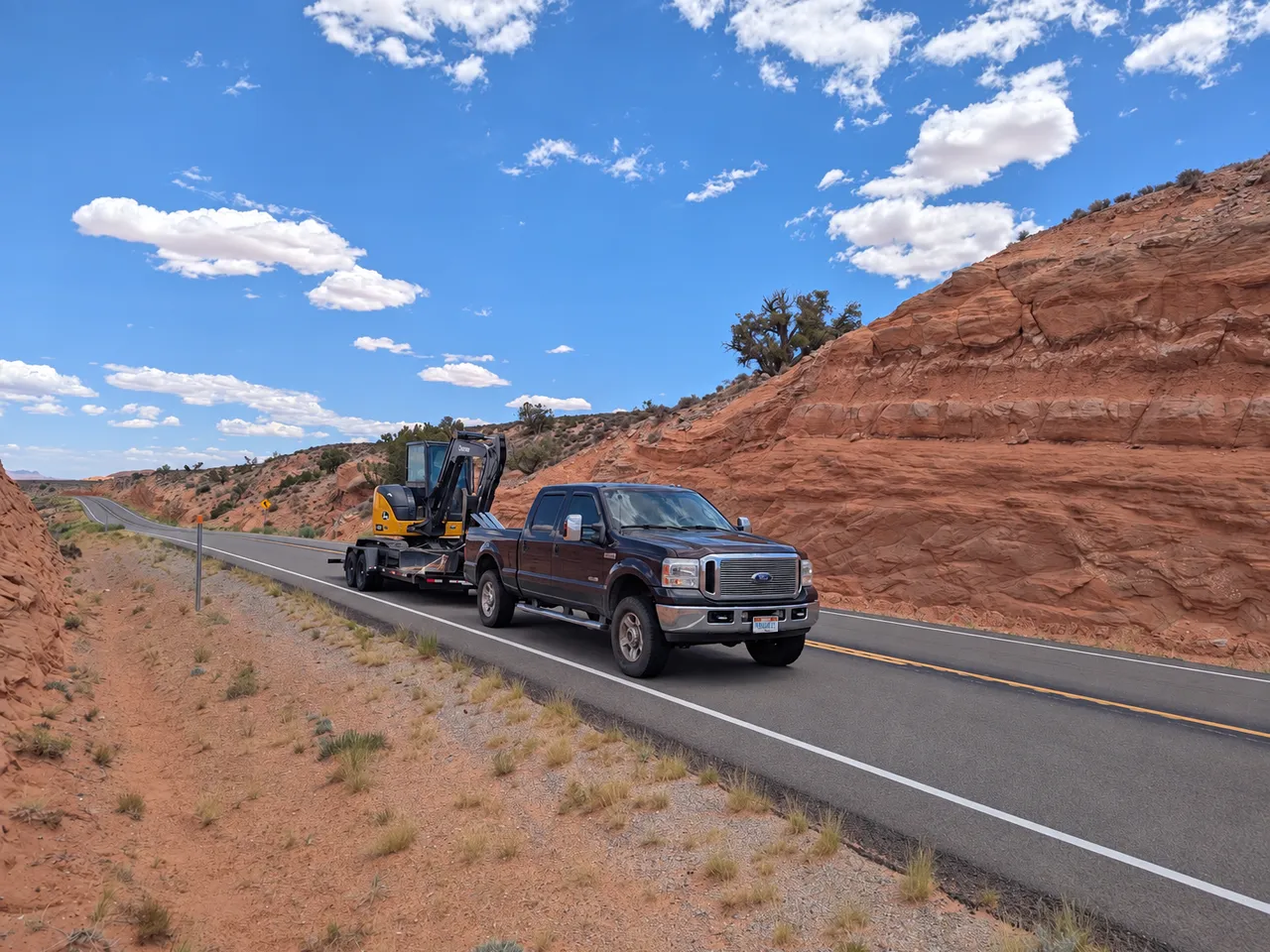 John Deere 50P transported on a trailer behind a pickup on a red-rock road